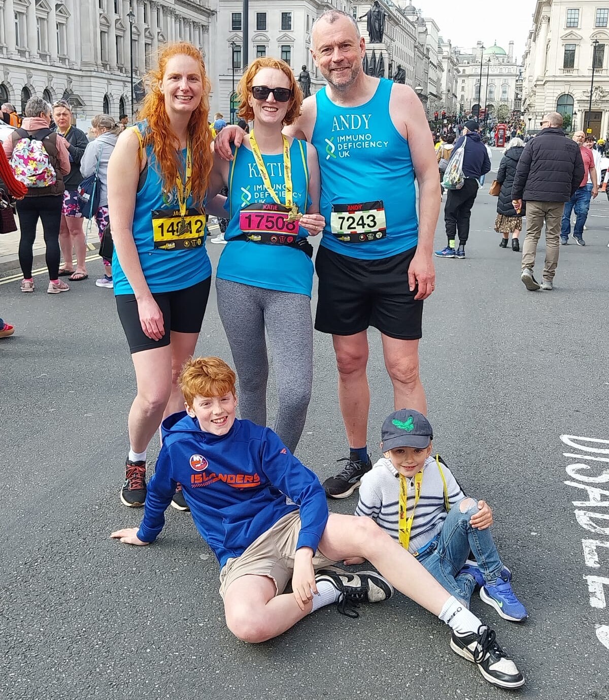 Three adults in running kit standing with two children laying on the ground